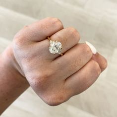 a woman's hand holding an engagement ring with a diamond in the middle, on top of her finger