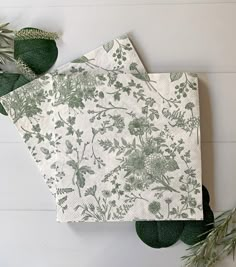 two napkins sitting on top of each other next to green leaves and plants in front of them