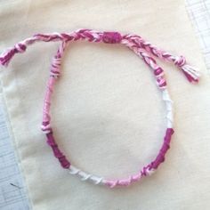 a pink and white string bracelet sitting on top of a piece of cloth