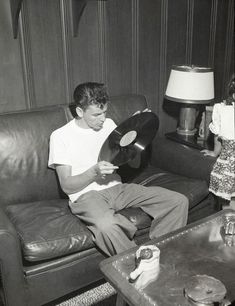 black and white photograph of a man sitting on a couch with a record in his hand