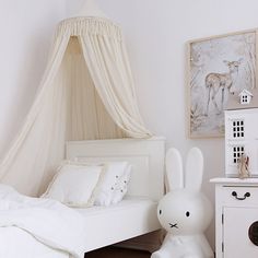 a white bed sitting next to a wooden dresser under a canopy over it's headboard