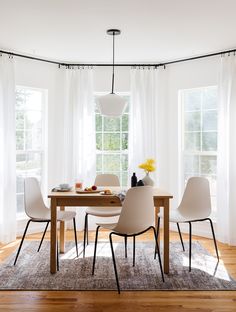 a dining room table with white chairs and a rug in front of the window,