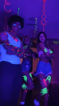 three young women dancing in the dark with neon colors on their body and arms,