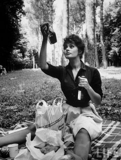 black and white photograph of woman sitting on blanket with picnic bag, bottle in hand