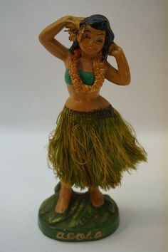 a figurine of a woman wearing a grass skirt with her hands on her head