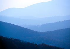 the mountains are covered in fog and blue hues as seen from an overlook point