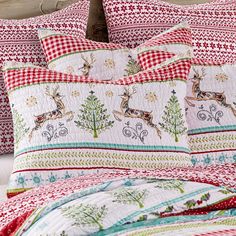 a bed covered in red and white quilts next to a night stand with two lamps on it