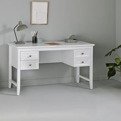 a white desk with two drawers and a potted plant in the corner next to it