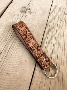 a leather keychain with an intricate design on the front and back side, resting on a wooden surface