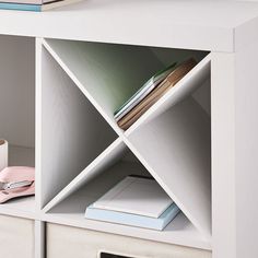 a white book shelf with books and other items on it's shelves next to a cup