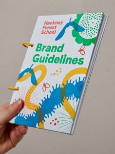 a hand holding a binder with the words brand guidelines written on it, in front of a white background