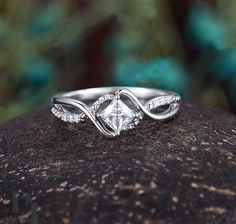 a white gold engagement ring with a princess cut diamond in the center on top of a rock