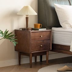 a nightstand with a cup on it next to a bed and a plant in the corner