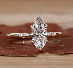 an oval cut diamond ring on top of a wooden surface with leaves in the background