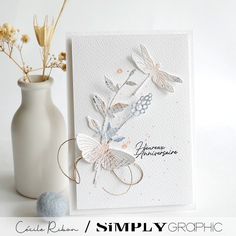 a white vase filled with flowers next to a greeting card that says simply graphic on it