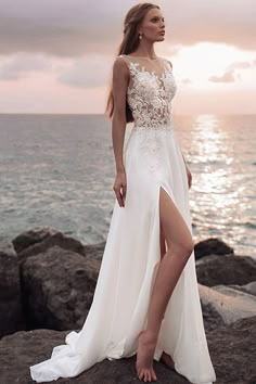 a woman in a white dress standing on rocks near the ocean with her leg up