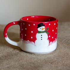 a red and white mug with a snowman painted on the inside is sitting on a table