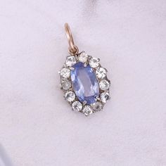 An antique charm featuring a 1.00ct natural moderate blue sapphire with a halo of diamond simulants set in silver topped 10k rose gold. The piece (circa 1920) measures 0.8 inches by 0.4 inches wide and weighs 1.24 grams. It is in great condition.  Each piece is shipped in a kraft box tied with a silk ribbon, to be gifted or as sweet treat for yourself. We work to send out items quickly, insuring a speedy delivery. Follow us on Instagram for new items, shop updates, and a behind the scenes look at LumaBloom - https://www.instagram.com/lumabloom/ Antique Sapphire Jewelry, Vintage Sapphire Jewelry With Diamond Accents, Vintage Sapphire Jewelry With Center Stone, Antique Blue Sapphire Jewelry, Vintage Blue Jewelry With Halo Setting, Heirloom Blue Jewelry With Diamond Accents, Antique Sapphire Gemstone Jewelry, Vintage Sapphire Birthstone Jewelry, Victorian White Gold Jewelry With Halo Setting