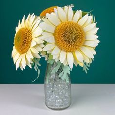 three yellow sunflowers in a glass vase on a white countertop against a green background