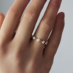 a woman's hand wearing a gold ring with three small white stones on it