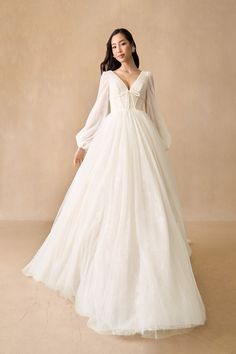 a woman in a white wedding dress standing on a beige background with her arms behind her back