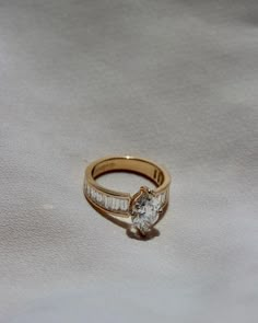 a gold ring with a single diamond on it sitting on a white cloth covered surface