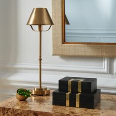 a table with two boxes and a lamp on it next to a framed mirror in a room