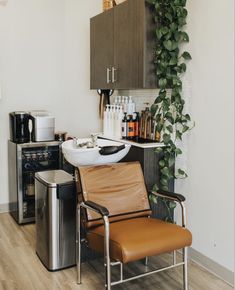 A caramel shampoo chair with white wash bowl stand in front of shampoo station and mini fridge. Shampoo Bowl And Chair, Wall Mounted Shampoo Bowl, Small Salon Studio Decor, Salon Suite Furniture, 2 Station Salon Suite, Hair Salon Wash Station Ideas, Single Chair Salon Layout, Stylist Station Ideas Decor, Corner Salon Stations