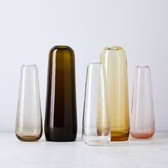 five different colored vases lined up in a row on a white countertop, one is empty