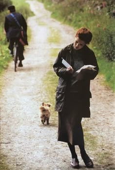 a woman walking down a dirt road next to a dog