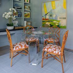 a glass dining table with four chairs in front of a painting on the wall behind it