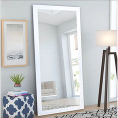 a large white mirror sitting on top of a wooden floor next to a lamp and table