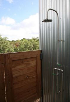 an open shower stall with a wooden door and metal siding on the side of it