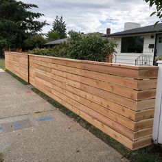 a wooden fence in front of a house with grass and bushes on the other side