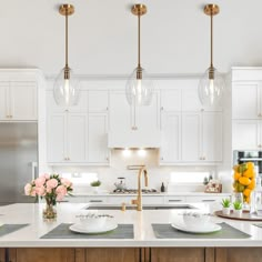 a large kitchen with white cabinets and marble counter tops, gold pendant lights over the island