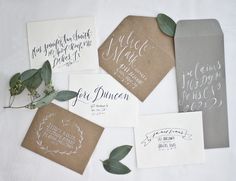 the wedding stationery is laid out on top of each other with greenery and calligraphy