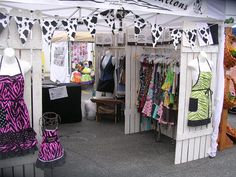 an outdoor market with clothes on display and cow print fabric hanging from the top of it