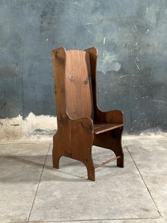 a wooden chair sitting on top of a cement floor next to a blue and gray wall