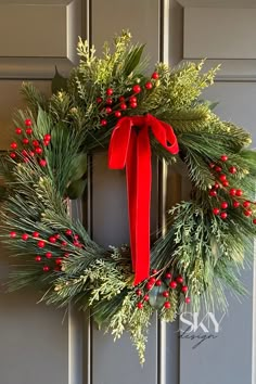 a christmas wreath with red berries and greenery hangs on the front door of a house