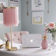 a white desk topped with a laptop computer next to a pink lamp and vase filled with flowers