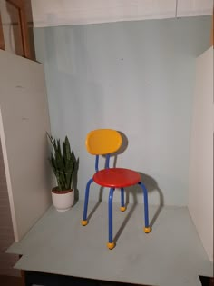 a red and yellow chair sitting on top of a white shelf next to a potted plant