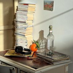 a desk with books, an orange and headphones sitting on it next to a bottle