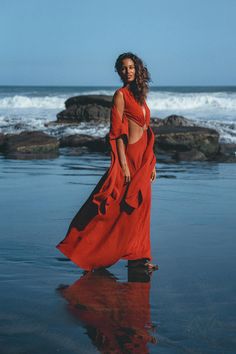 a woman in a red dress standing on the beach