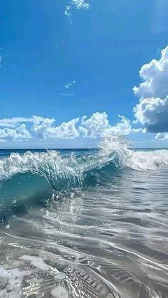 an ocean wave breaking on the beach under a blue sky with white clouds and sunbeams