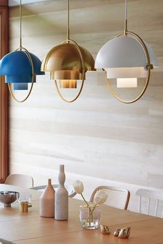 three pendant lights hanging over a wooden table with white chairs and vases on it