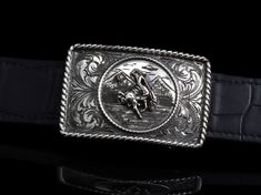 The Tyson R Bronc by Comstock Heritage is a hand crafted Sterling Silver trophy buckle with attention to detail. This buckle features a center piece of a bronc and rider (who's losing his hat in the ride) atop a hand engraved mountain scene, inside of a hand wrought small rope border. Surrounding the whole center scene is our classic Victorian engraving inside another, larger, Sterling rope edge. Measures 1 ¾" x 2 ⅝” Fits up to a 1 ¼" belt strap Classic Concho Belt Buckles For Rodeo, Western Style Antique Belt Buckle For Formal Wear, Western Style Antique Belt Buckle For Formal Occasion, Engraved Adjustable Belt Buckles For Rodeo, Adjustable Engraved Belt Buckles For Rodeo, Western Engraved Belt Buckles For Formal Wear, Western Silver Belt With Buckle, Western Silver Belt With Buckle Closure, Victorian Engraving