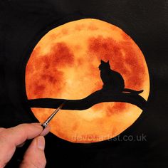 a person is painting a cat on a tree branch with the moon in the background