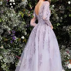 a woman standing in front of flowers wearing a lavender colored wedding dress with long sleeves