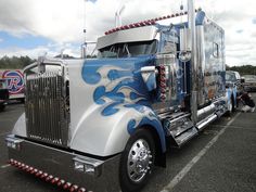 a blue and white semi truck with flames painted on it's side in a parking lot