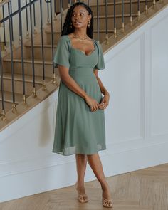 a woman standing in front of a staircase wearing a green dress with short sleeves and open shoulders